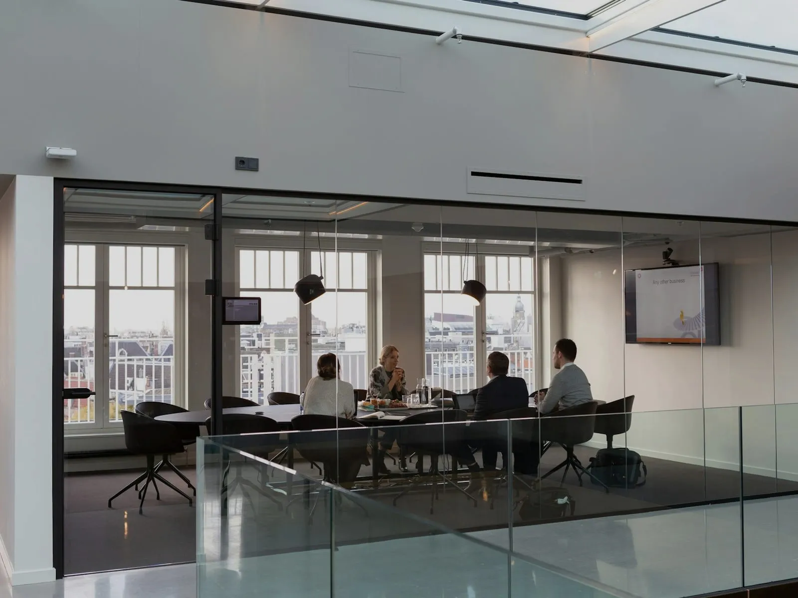 Four people in a meeting in a glass-walled conference room of a bright, modern office.